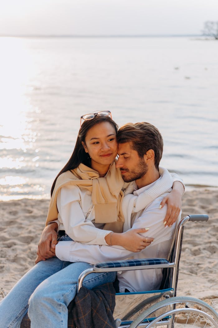 services-02 A loving couple shares an emotional moment at the seaside, one seated in a wheelchair.