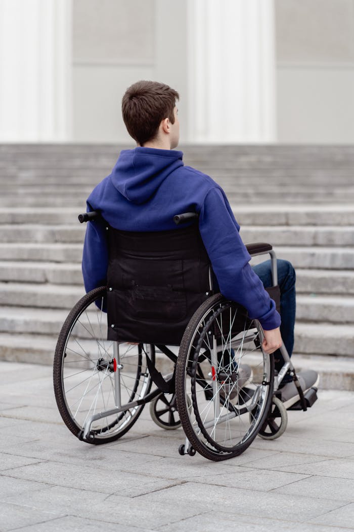 our-services-2 A young man in a wheelchair with a blue hoodie facing a staircase outdoors.