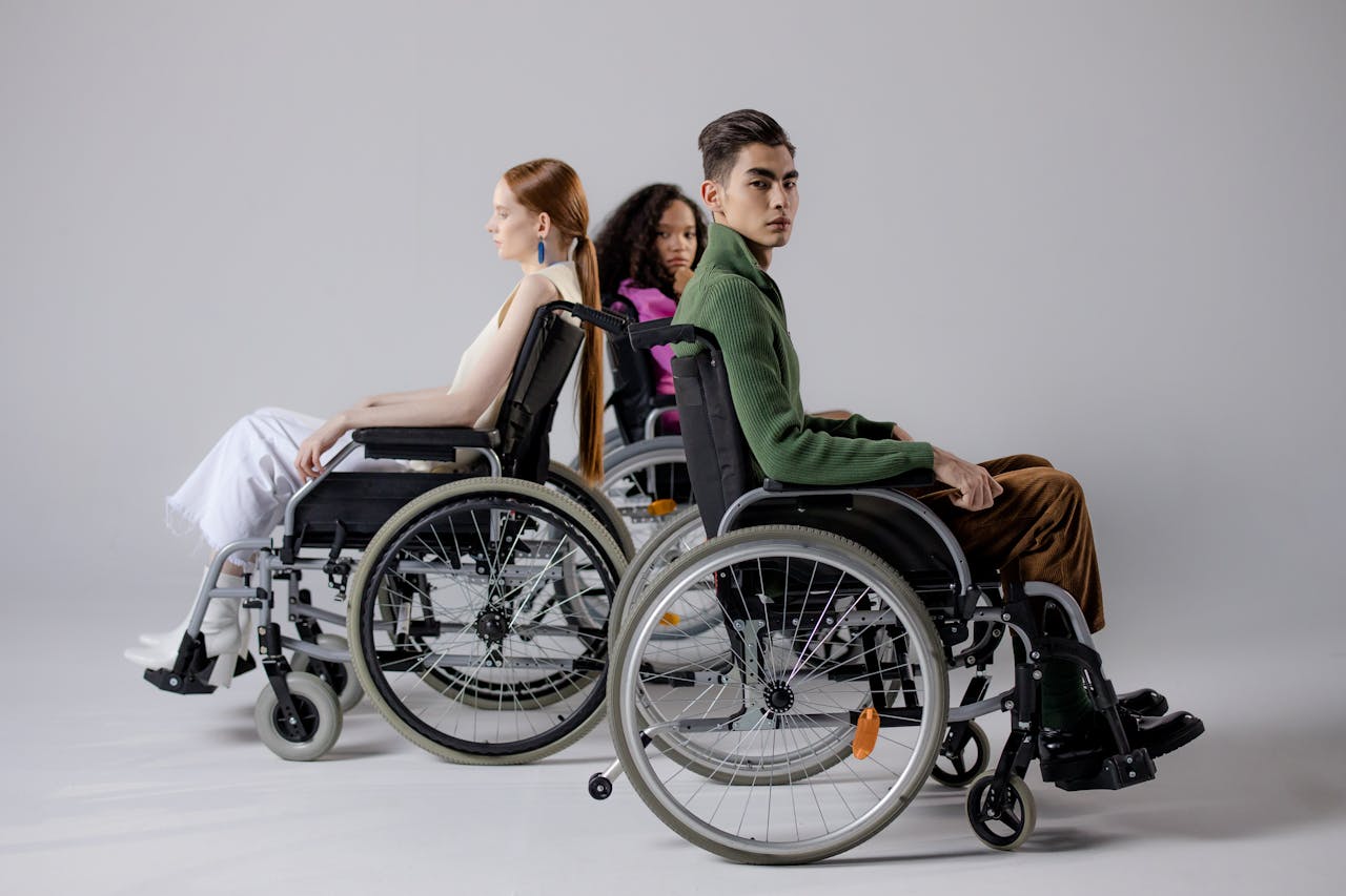 about-01 Three diverse individuals in wheelchairs posing indoors, symbolizing inclusivity.